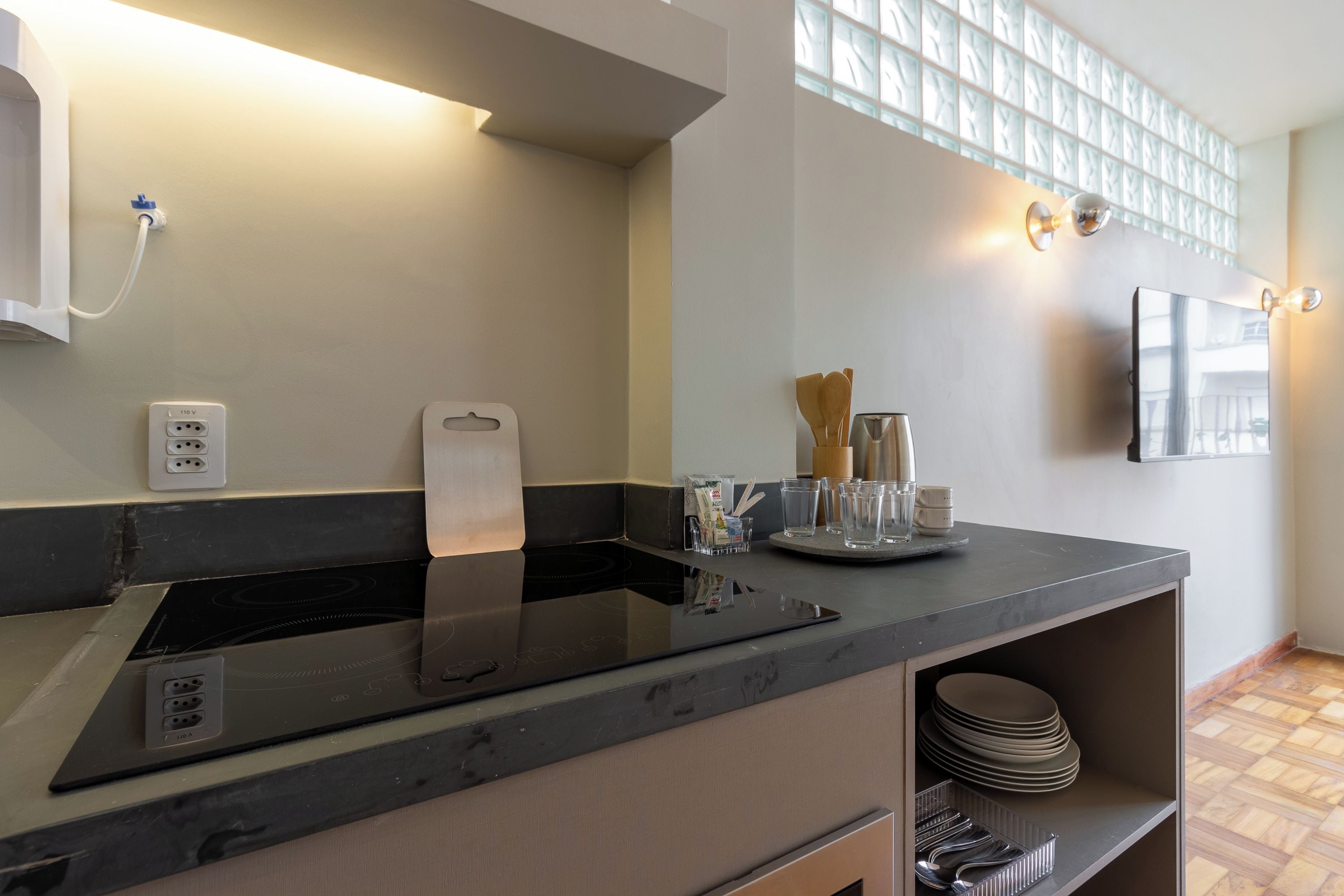 A modern kitchen with a built-in induction cooktop, a countertop with glassware and a tea kettle, and a wall-mounted light fixture.