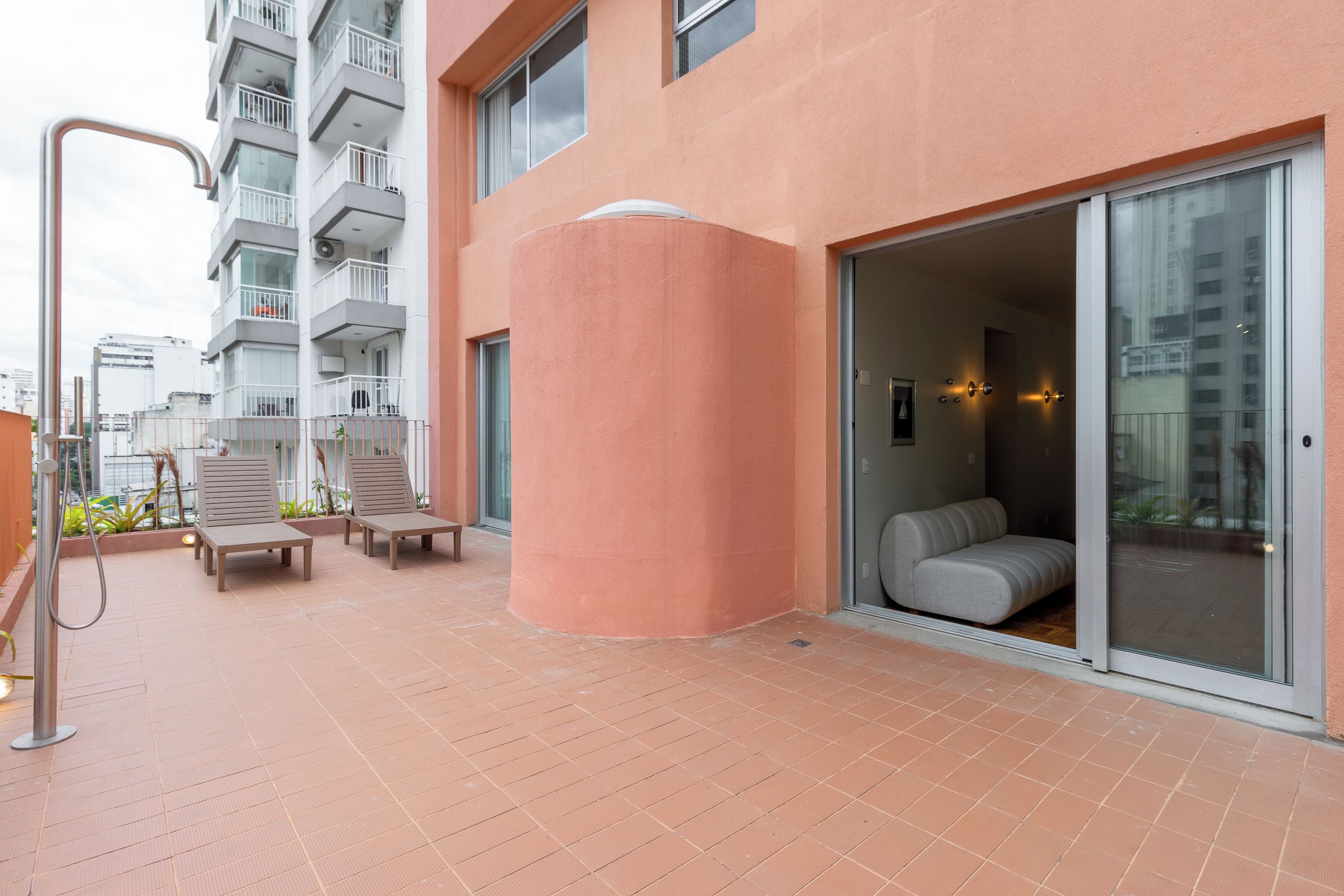 A modern building with a pink facade, a covered outdoor seating area with chairs, and a glass door entrance.