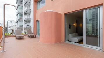 A modern building with a pink facade, a covered outdoor seating area with chairs, and a glass door entrance.