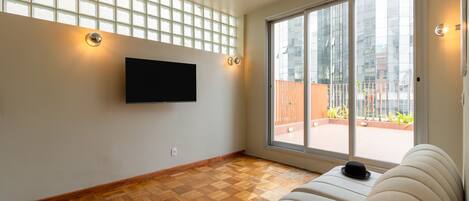 A living room with a flat-screen TV mounted on the wall, a sofa, and a large sliding glass door leading to an outdoor area.