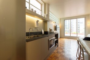 Una cocina moderna con horno empotrado, un lavamanos y un ventanal con vistas a un paisaje urbano.