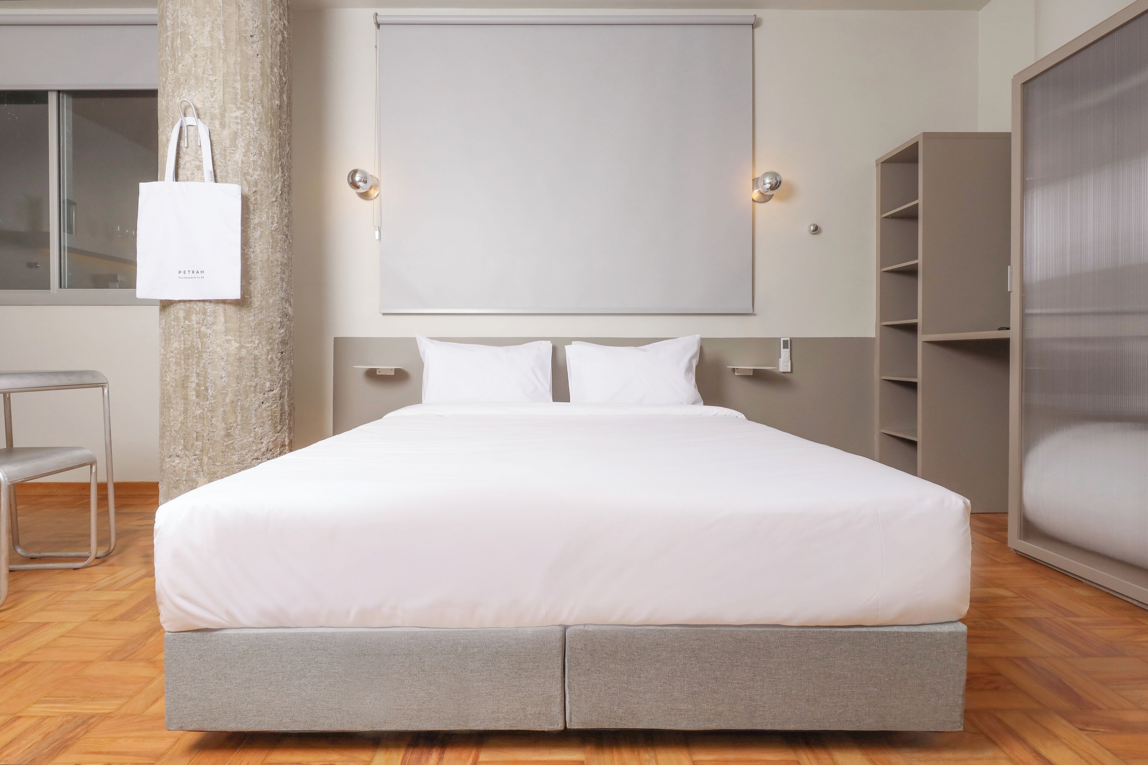 Une chambre moderne avec un grand lit, une armoire, une chaise et un luminaire fixé au mur.