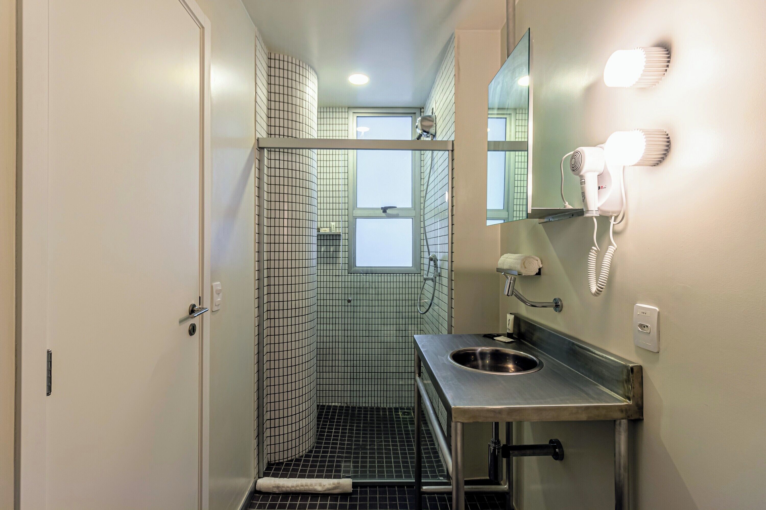 A compact bathroom with a shower, a sink, a mirror, and a hairdryer mounted on the wall.