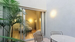 A patio with a table and chairs, a potted plant, and a sliding glass door leading to a bedroom. - Charlie Petrah Vila Buarque - Soft Opening (São Paulo)