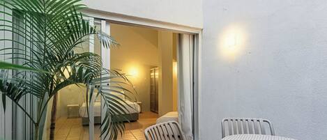 A patio with a table and chairs, a potted plant, and a sliding glass door leading to a bedroom.