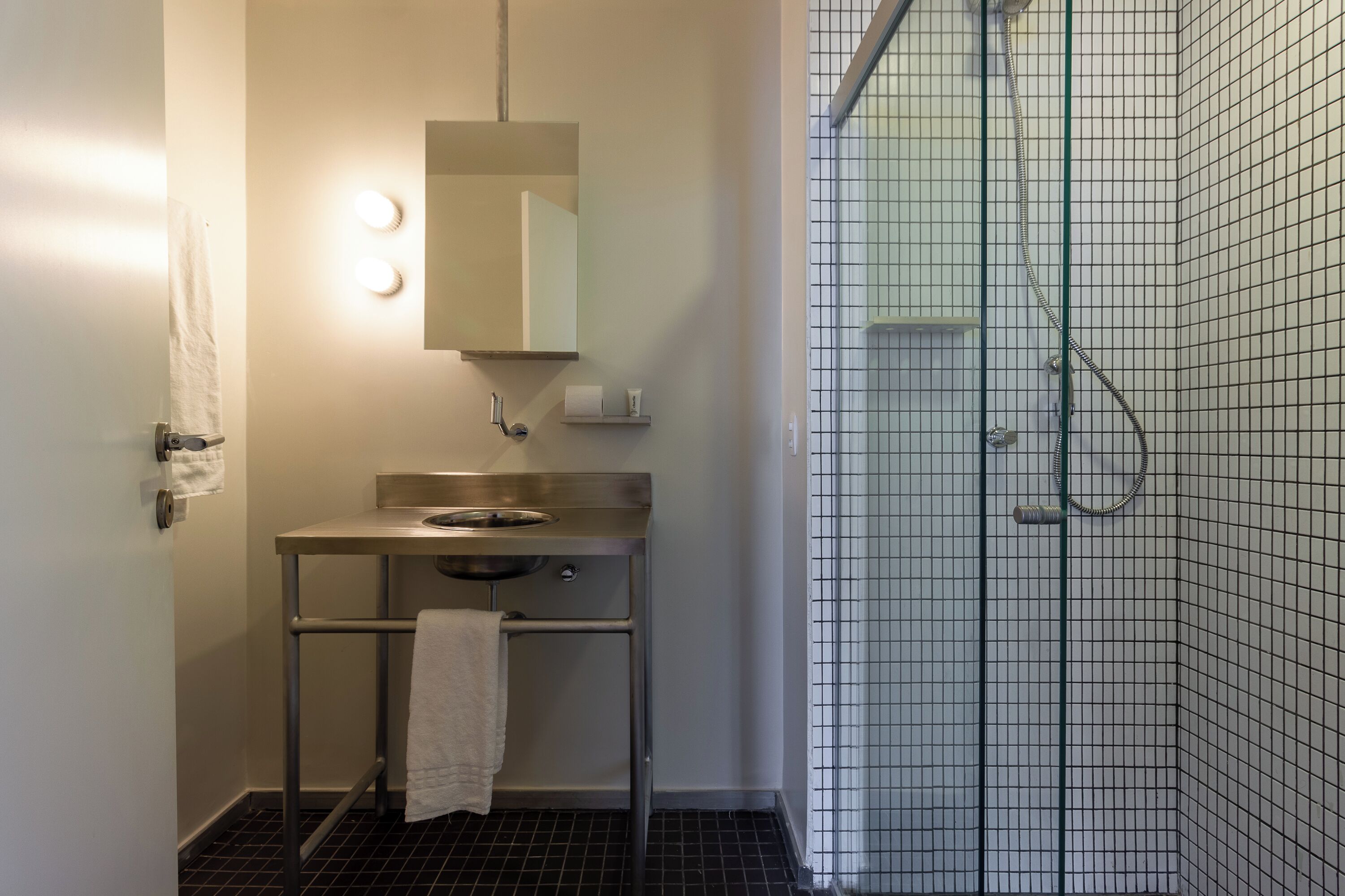 Baño con lavamanos, espejo, toallero y zona de ducha con paredes de azulejos.