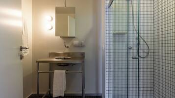 Baño con lavamanos, espejo, toallero y zona de ducha con paredes de azulejos.
