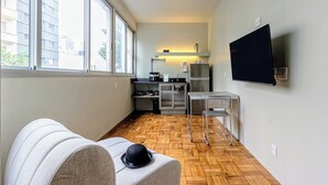 A compact living space with a kitchenette, a sofa, a television, and large windows. - Charlie Petrah Vila Buarque - Soft Opening (São Paulo)