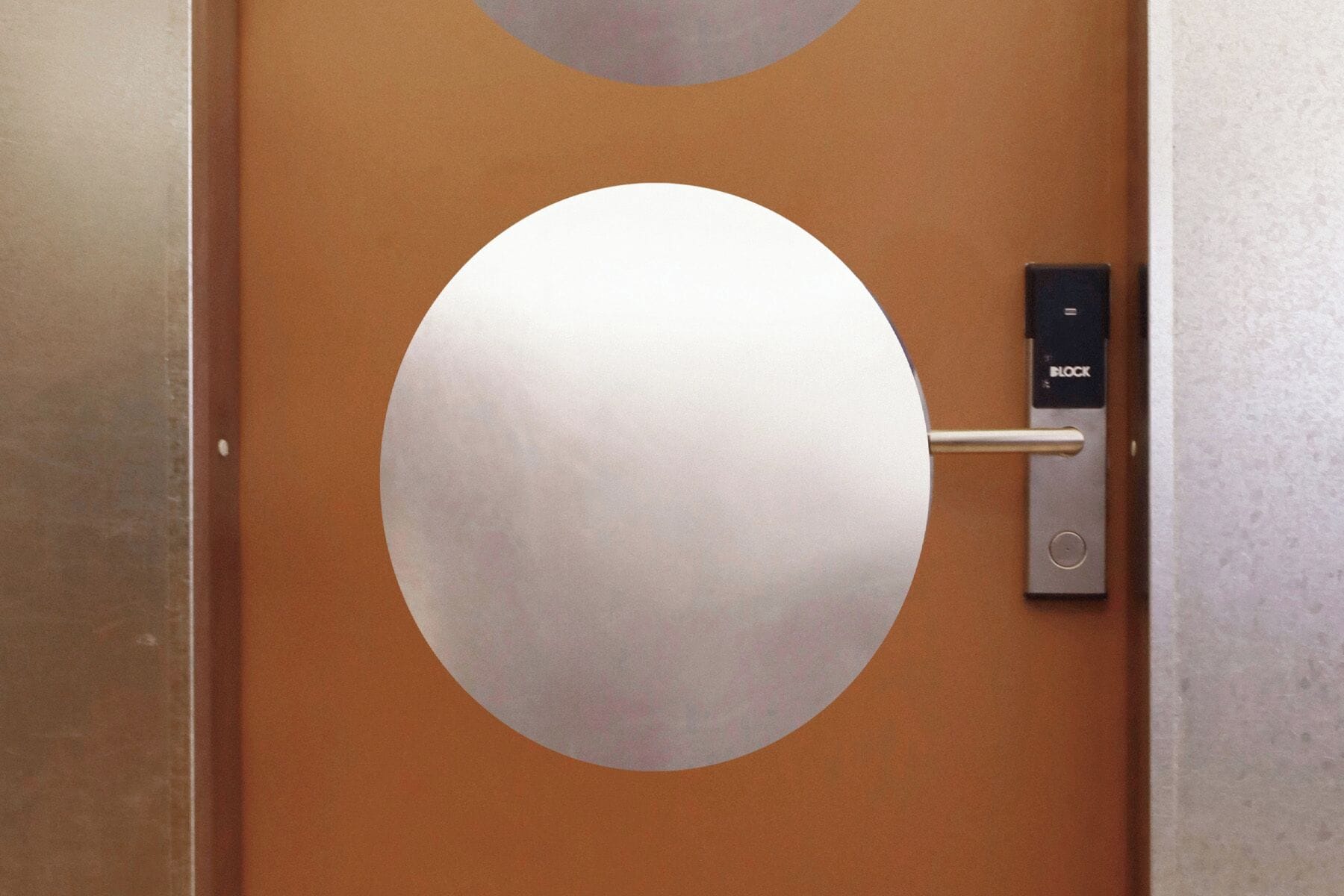 Une porte dotée d’une grande ouverture circulaire, d’une poignée métallique et d’un mécanisme de verrouillage.