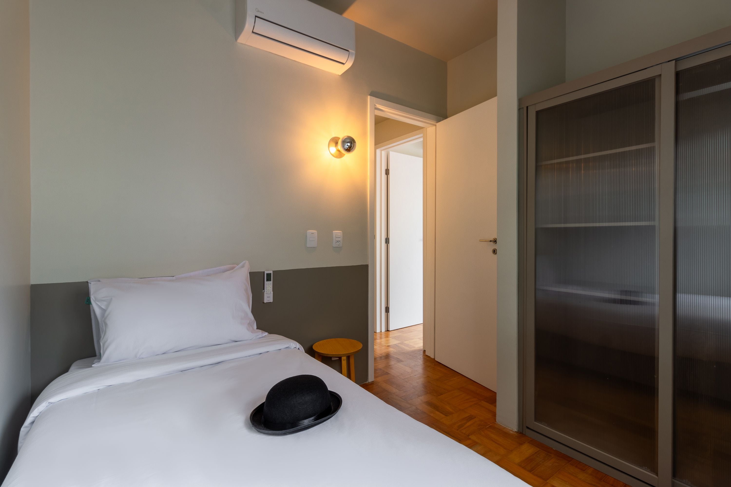 A hotel room with a bed, a bedside table, a wall-mounted air conditioner, and a sliding door closet.