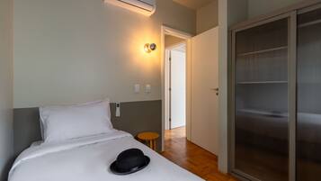 A hotel room with a bed, a bedside table, a wall-mounted air conditioner, and a sliding door closet.