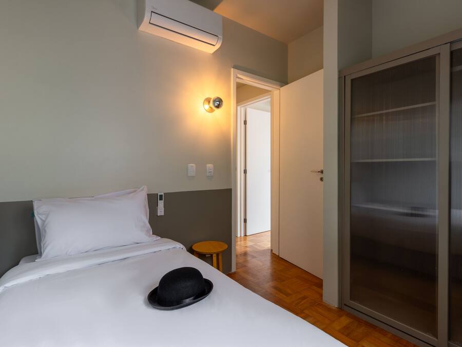 A hotel room with a bed, a bedside table, a wall-mounted air conditioner, and a sliding door closet.