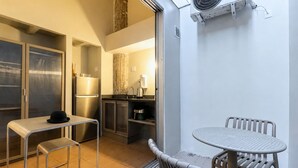 A compact kitchen with a refrigerator, stove, and sink. There is a small dining table with chairs and a single hanging light fixture. - Charlie Petrah Vila Buarque - Soft Opening (São Paulo)