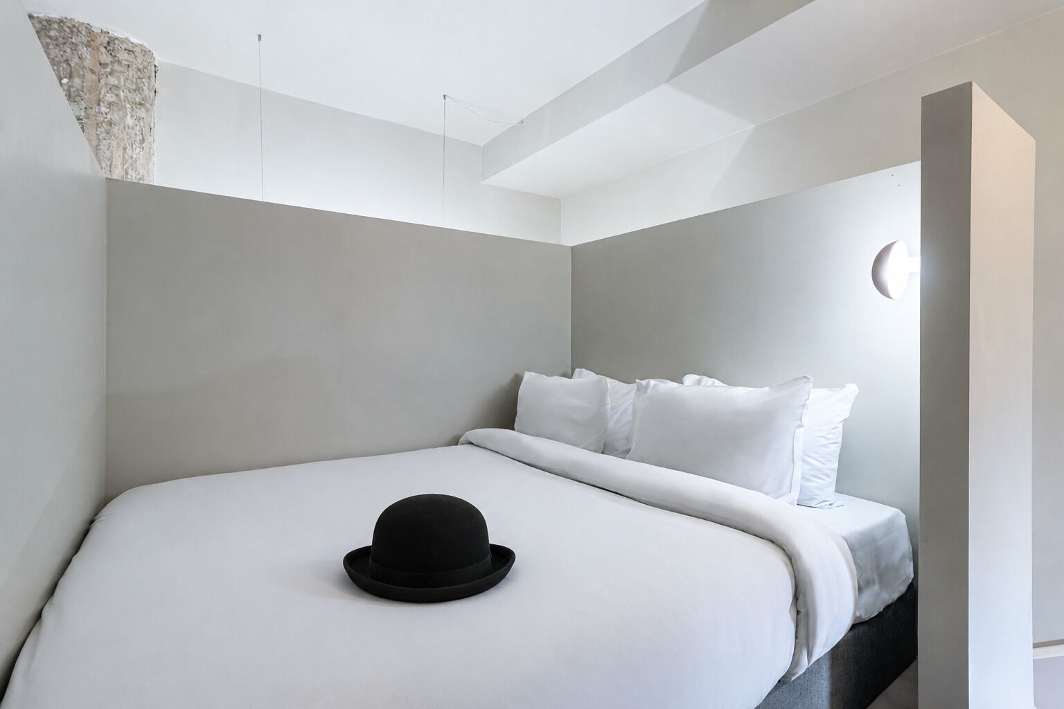 A modern hotel room with a bed, a black hat on the bed, and a light fixture on the ceiling.