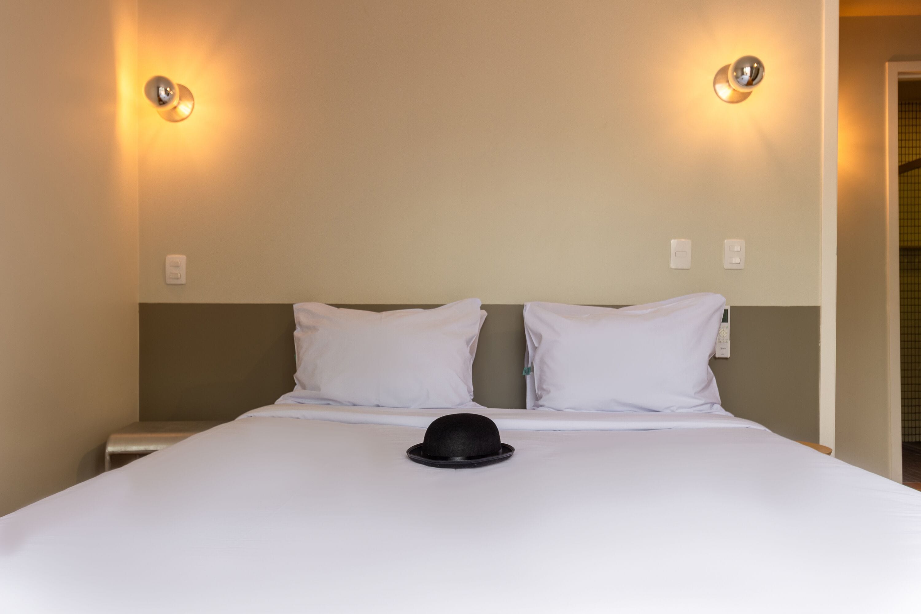 Habitación de hotel con cama, dos lámparas de pared y una puerta a la derecha.