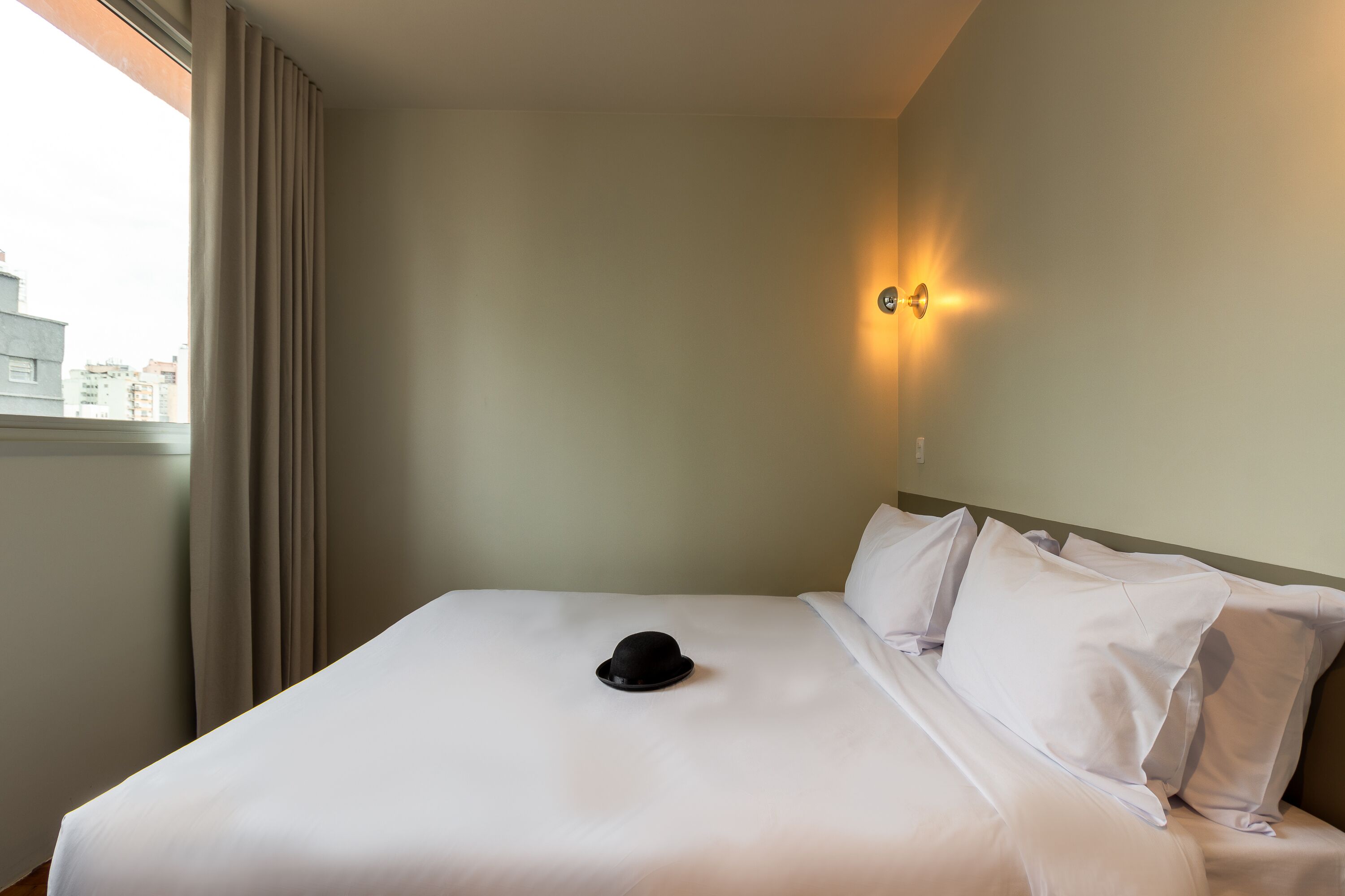 A hotel room with a bed, a hat on the bed, and a wall-mounted light.