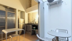 A compact kitchen with a refrigerator, stove, and cabinets, a small dining table with chairs, and a sliding glass door leading to an outdoor area. - Charlie Petrah Vila Buarque - Soft Opening (São Paulo)