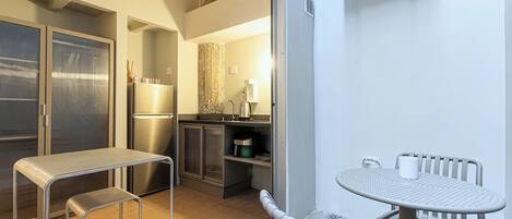 Cocina compacta con refrigerador, estufa y armarios, una pequeña mesa de comedor con sillas y una puerta corrediza de vidrio que da a un área exterior.