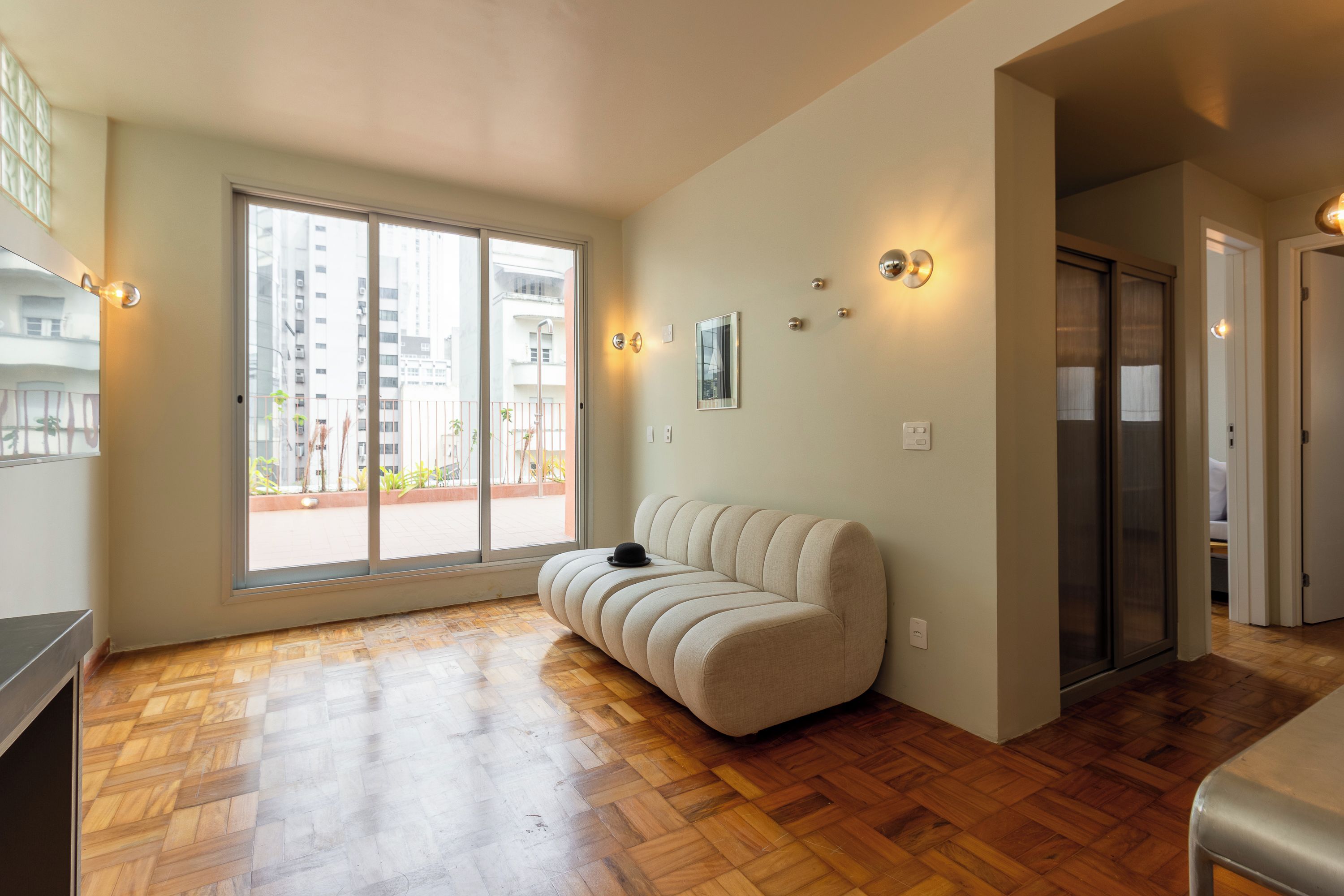 Un salon moderne avec un canapé, une grande porte-fenêtre coulissante et une vue sur le paysage urbain.
