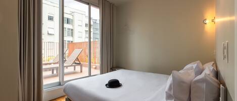 A hotel room with a bed, a hat on the bed, a window with curtains, and a view of the outside balcony.