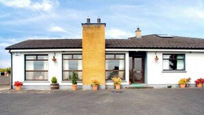 A single-story building with a brick chimney, large windows, and potted plants along the front. - 2 Bed in Ballybay (oc-ii04618) (Ballybay)