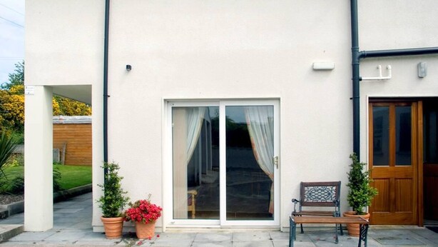 A building with a white exterior, a sliding glass door, a wooden door, a bench, and potted plants. - 2 Bed in Ballybay (oc-ii04618) (Ballybay)