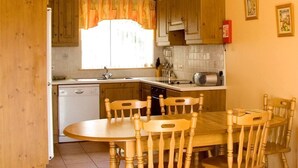 A kitchen with wooden cabinets, a dining table with chairs, a window with curtains, and a fire extinguisher on the wall. - 2 Bed in Ballybay (oc-ii04618) (Ballybay)