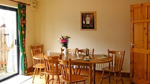 Un coin repas avec une table ronde, des chaises en bois, un vase de fleurs et un tableau encadré au mur.