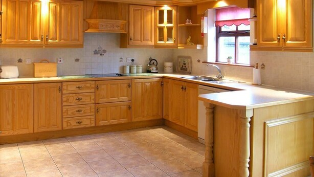 Une cuisine avec des meubles de rangement en bois, un plan de travail, un évier et une fenêtre avec un rideau.