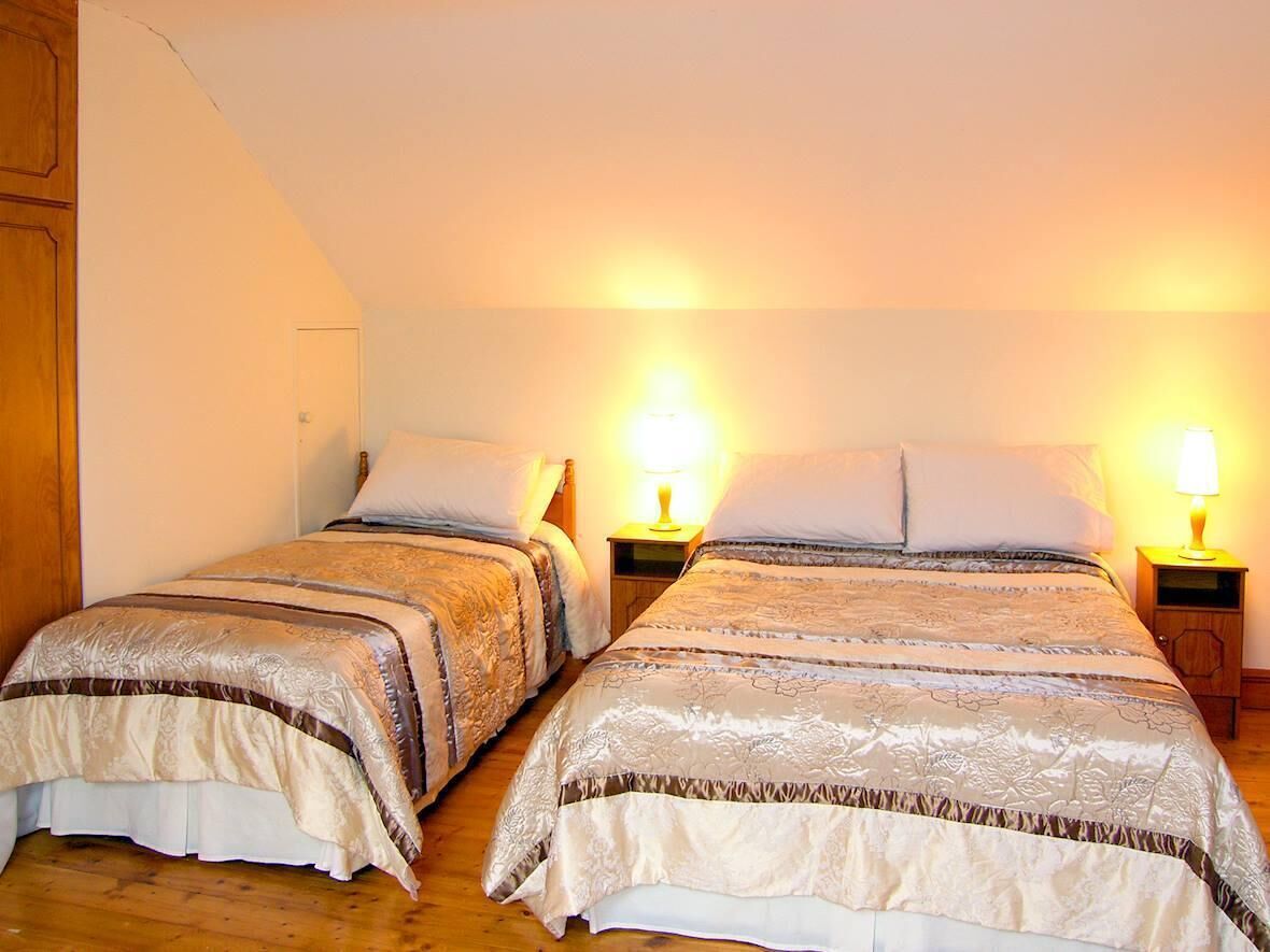 Two double beds with matching headboards, bedside tables with lamps, and a wooden floor.