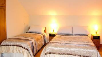 Two double beds with matching headboards, bedside tables with lamps, and a wooden floor.
