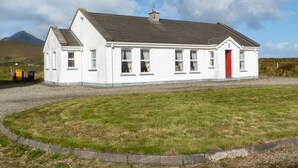 A white building with a red door, windows, and a chimney. - 3 Bed in Achill Island (oc-ii06848) (Doogort)