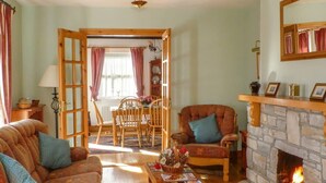 A cozy living room with a fireplace, a dining area with a table and chairs, and a comfortable sofa. - 3 Bed in Achill Island (oc-ii06848) (Doogort)