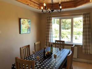 A dining area with a table set for four, a chandelier, a window with curtains, and a painting on the wall. - 5 Bed in Clifden (oc-ii05854) (Leagun)