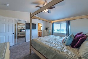 Uma cama com dossel, um ventilador de teto, um espelho grande e vista para a cozinha através de uma porta aberta.