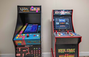Duas máquinas de arcade, uma com a inscrição 'Arcade 1UP' e a outra 'Midway Mortal Kombat'.