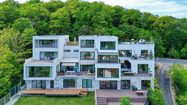 Un bâtiment moderne à plusieurs étages, doté de grandes fenêtres, d’espaces extérieurs aménagés pour s’asseoir et entouré d’une forêt.