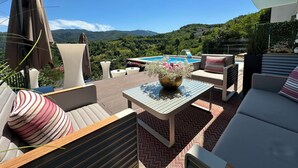 Une terrasse avec des sièges extérieurs, une piscine et un paysage montagneux en arrière-plan.