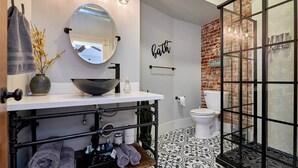 Une salle de bain avec un miroir rond, un lavabo sur colonne, des toilettes et un espace douche doté d’une porte en verre.