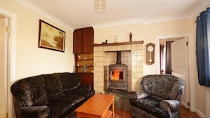 Una sala de estar con chimenea, dos sofás, una mesa de centro de madera y un reloj en la pared.