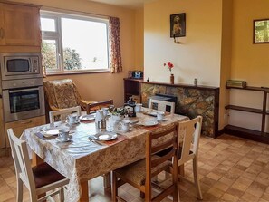 A dining area with a table set for four, a microwave, oven, and a stone fireplace. - 3 Bed in Rosscarbery (oc-ii16117) (Rosscarbery)
