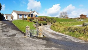 Il s’agit d’une propriété résidentielle dotée d’une allée menant à une entrée fermée par un portail, d’une maison avec un toit en pente et d’un terrain verdoyant.