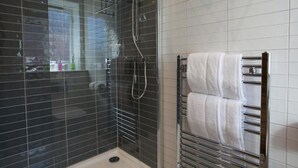 Une salle de bain moderne avec une douche à parois de verre, un mur recouvert de carreaux blancs et un porte-serviettes avec deux serviettes.