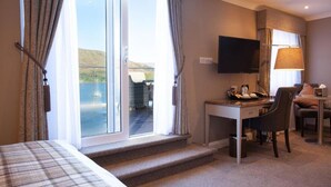 Une chambre d’hôtel comprenant un lit, un bureau avec une chaise, une télévision et une vue sur une étendue d’eau grâce à de grandes fenêtres.