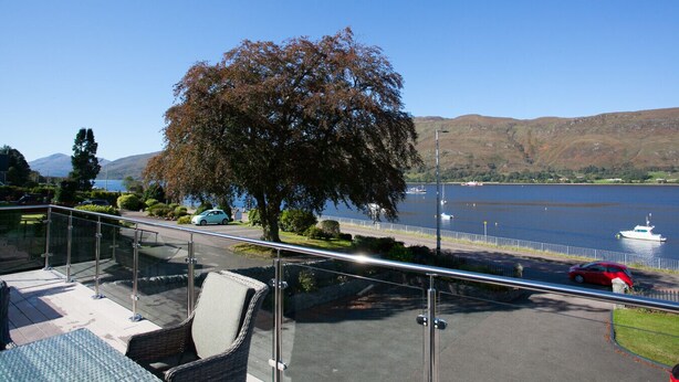 Un balcon doté d’une balustrade en verre, offrant une vue sur un lac, un arbre et, au loin, sur des collines.