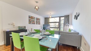 Ein modernes Wohnzimmer mit Essbereich, einem grauen Sofa und einem Fernseher auf einem Lowboard.