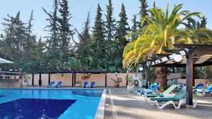 Une piscine avec des chaises longues, une pergola et un décor de verdure.