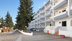 Un immeuble résidentiel à plusieurs étages, doté de balcons, d’un espace de stationnement et situé dans une rue bordée d’arbres.