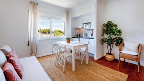 Une pièce moderne et bien éclairée, comprenant un coin repas, une cuisine et un espace salon agrémenté d’une plante.