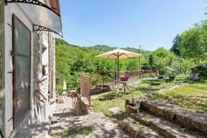 A stone building with a covered outdoor seating area, a staircase, and a view of a green hillside. - Holiday Home 'La Casa Di Pietra - Maissana' with Mountain View, Private Terrace and Private Garden (Varese Ligure)